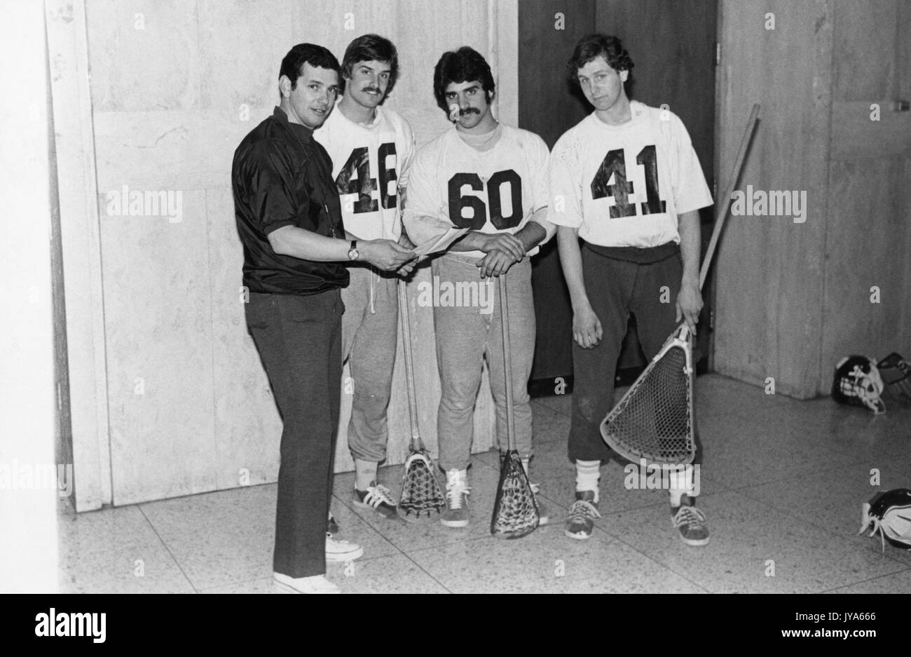Un ritratto a lunghezza intera di un allenatore di lacrosse della Johns Hopkins University Henry Ciccarone che discute di strategia con due giocatori di campo lacrosse e un goalie, in piedi con i loro bastoni lacrosse in mano, al Ralph S. o'Conner Recreation Center presso la Johns Hopkins University, Baltimora Maryland. 1976. Foto Stock