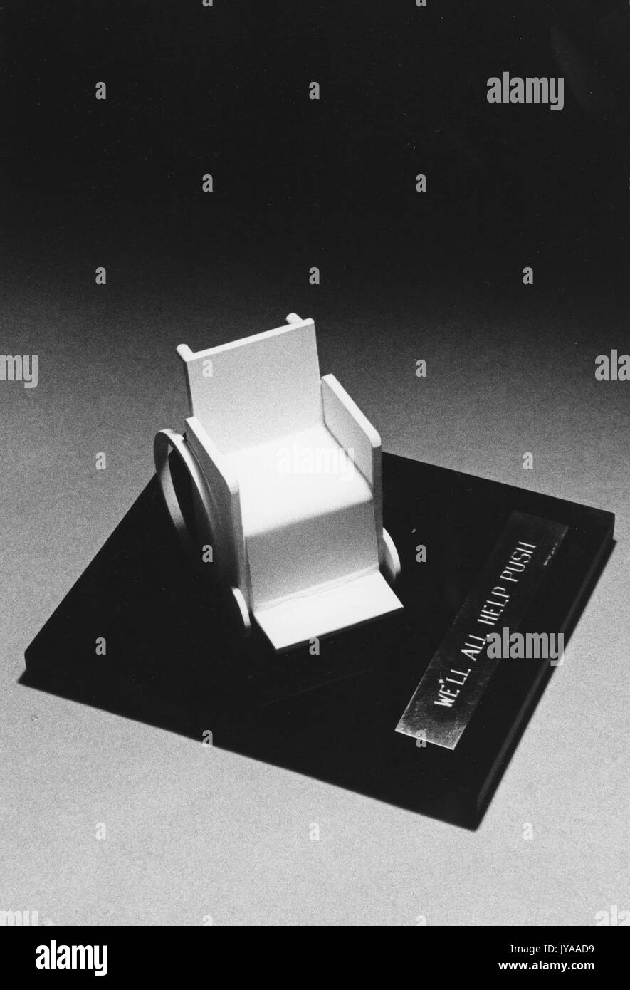 Una sedia a rotelle in miniatura su una placca di legno con il titolo "NOI TUTTI AIUTEREMO A SPINGERE", MSE Symposium, 1970. Foto Stock