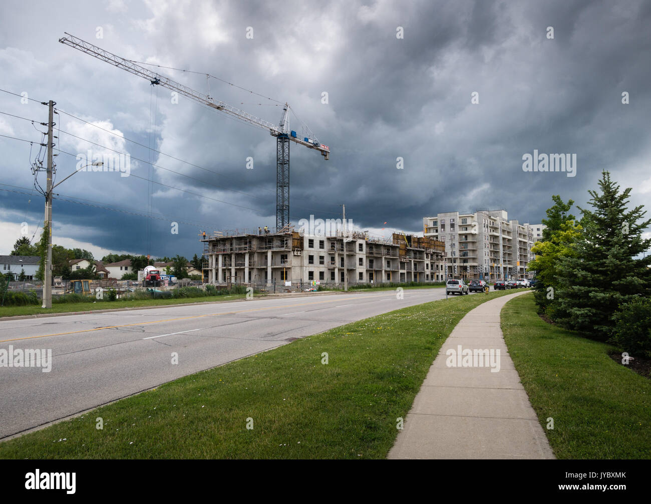 Nuvole temporalesche approccio gru e dei lavoratori sul tetto di un edificio in corrispondenza di un sito in costruzione Foto Stock