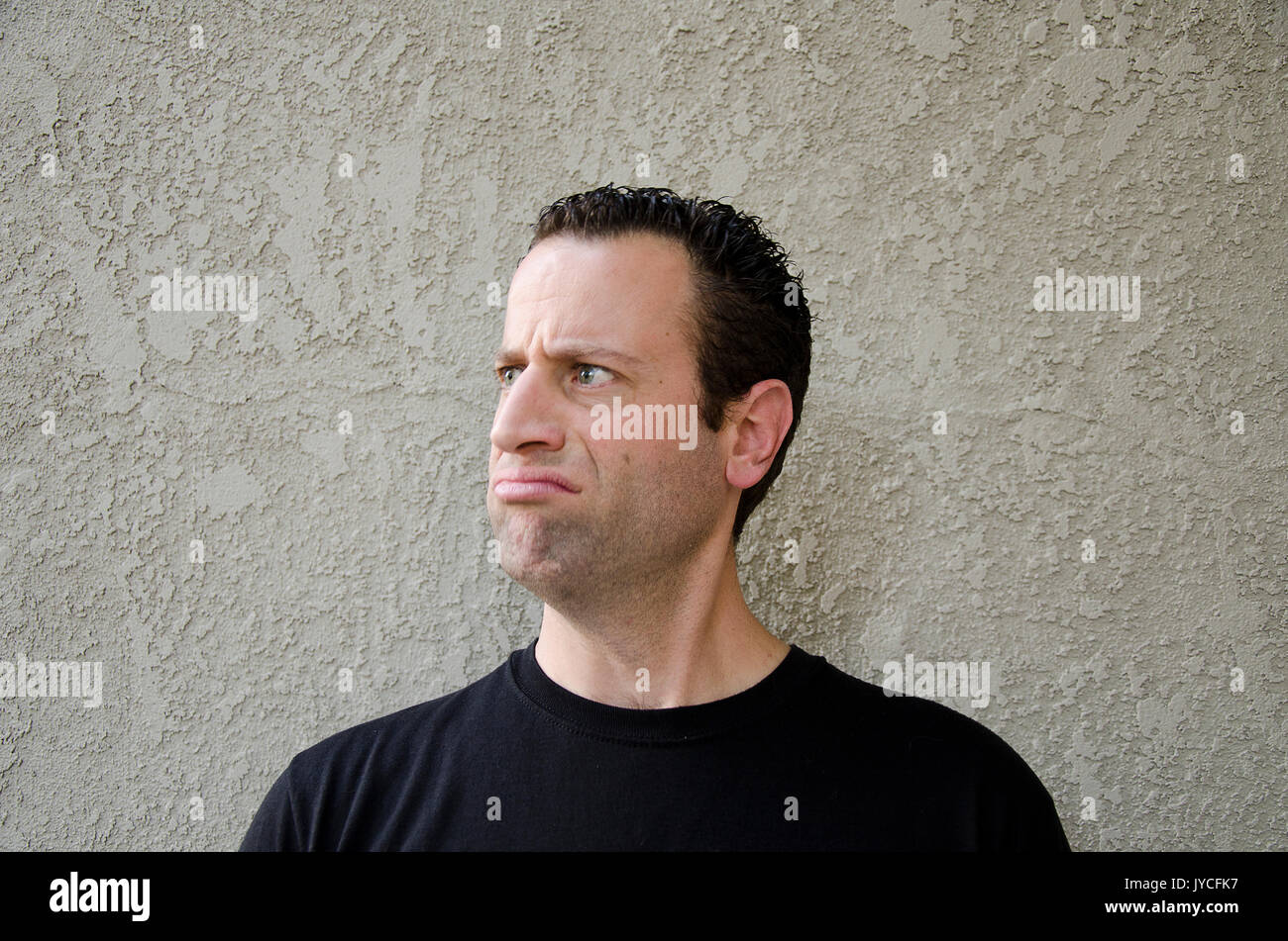 Uomo di fronte a un sfondo beige facendo una faccia insoddisfatti guardando a sinistra. Foto Stock