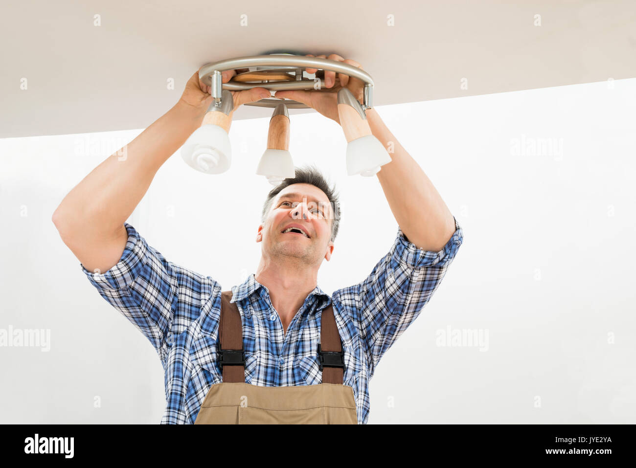 Ritratto di un elettricista maschio che fissa la luce sul soffitto Foto Stock