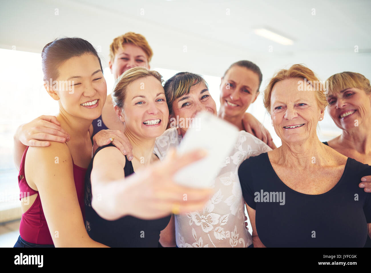 Mescolò età gruppo di donne che ridono in piedi a braccetto prendendo un selfie tgether in uno studio di danza Foto Stock