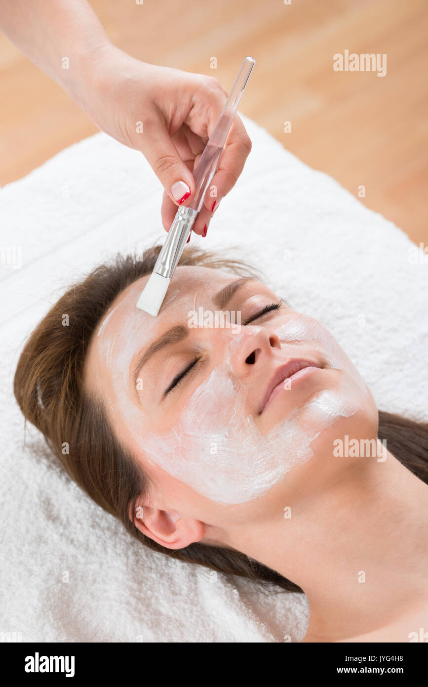 Terapista mani con pennello applicare la maschera per il viso a una giovane donna in un centro termale Foto Stock