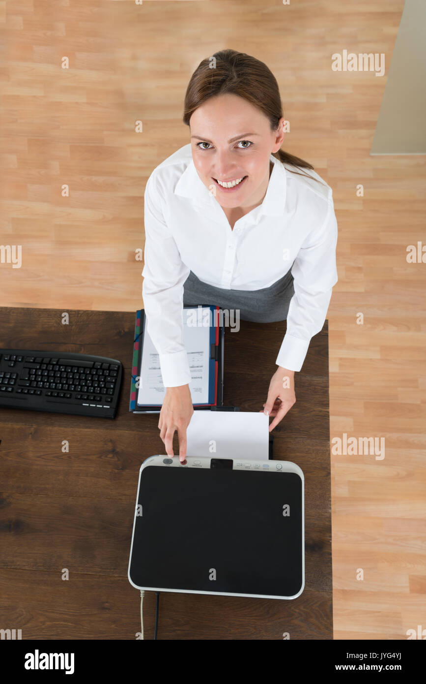 Angolo di Alta Vista del giovane imprenditrice utilizzando una stampante a scrivania in ufficio Foto Stock