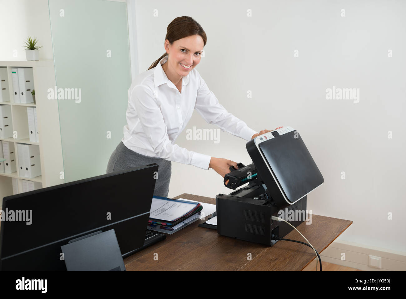 Giovane imprenditrice felice tenendo la cartuccia laser con stampante a scrivania Foto Stock