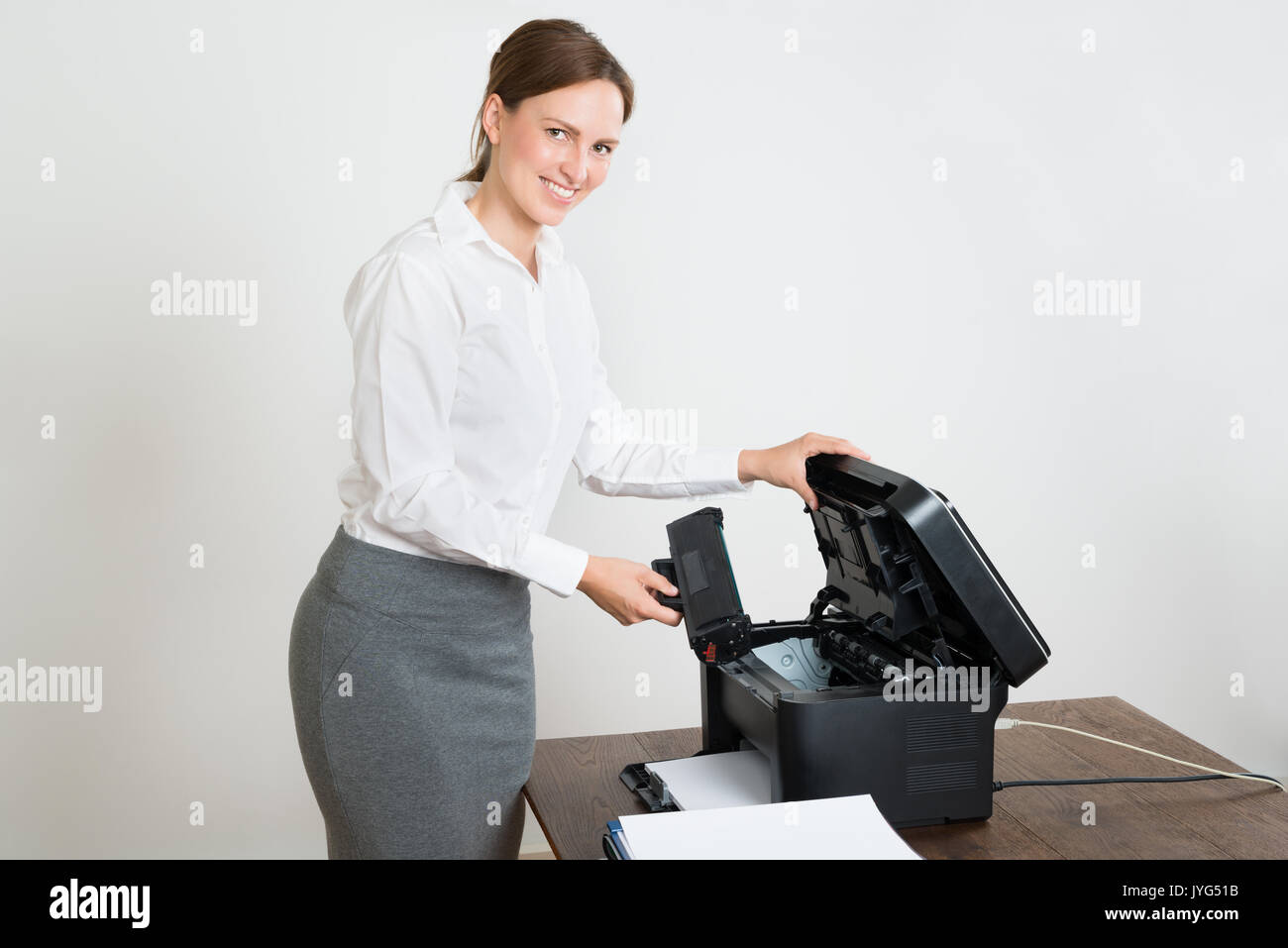 Giovane imprenditrice felice tenendo la cartuccia laser con stampante a scrivania Foto Stock