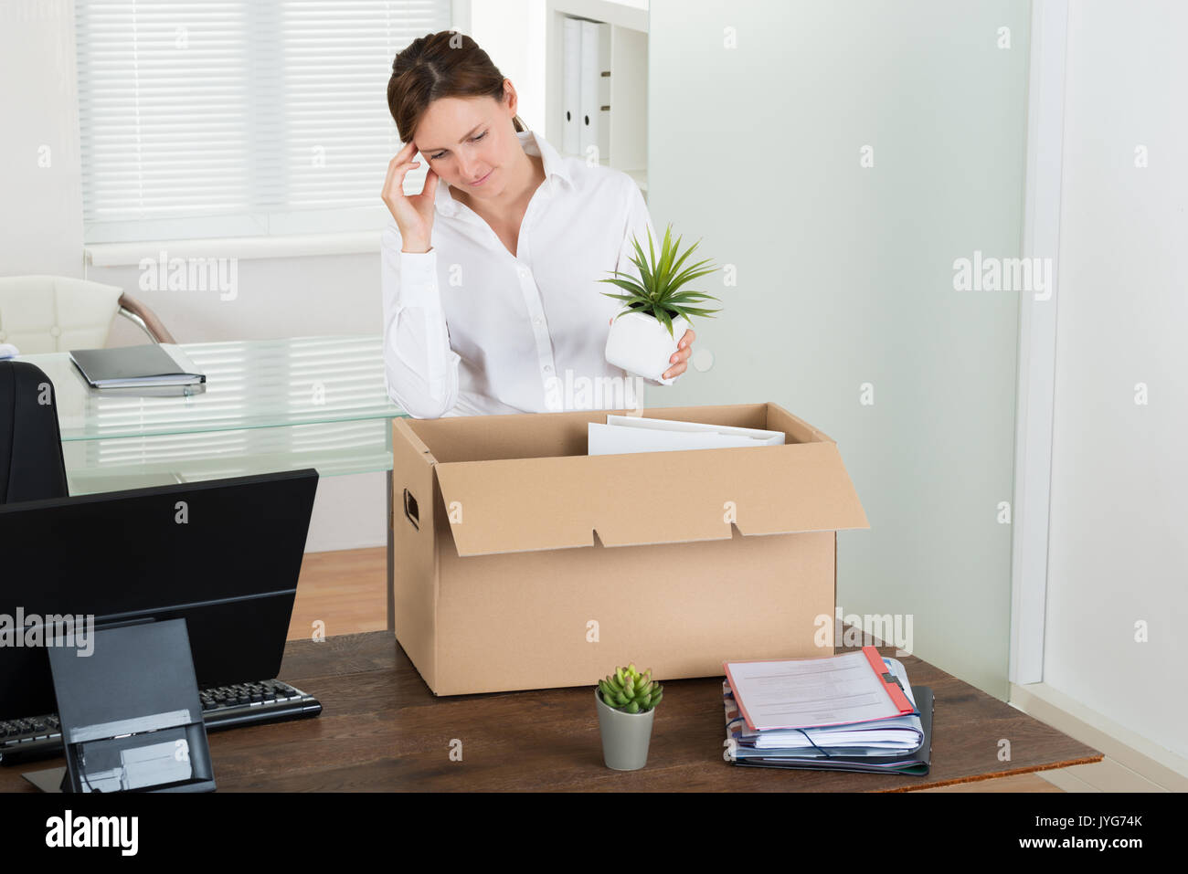 Giovane imprenditrice triste mettendo i suoi averi nel box alla scrivania in legno Foto Stock