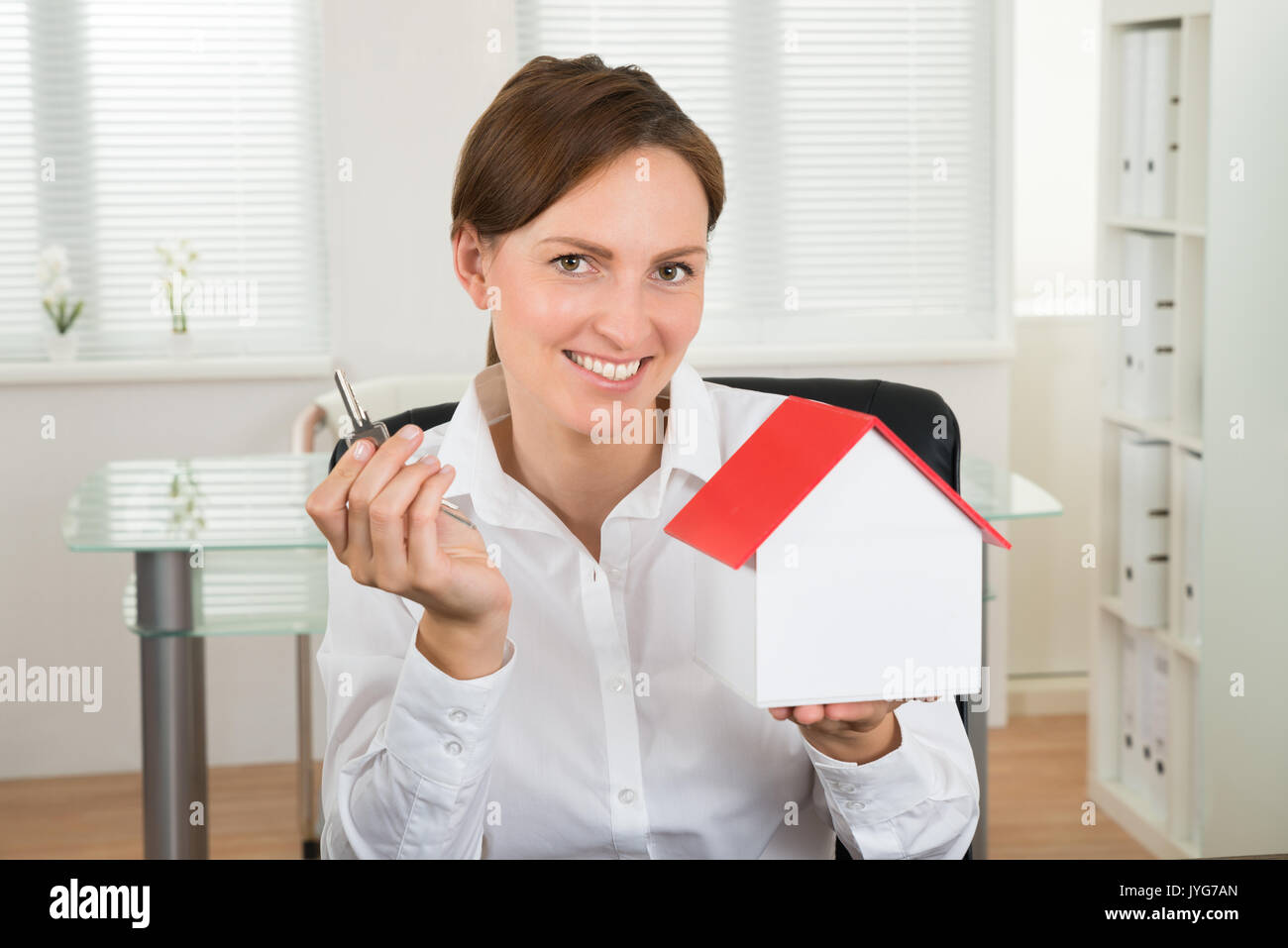 Felice imprenditrice in possesso della chiave e il modello della casa in ufficio Foto Stock