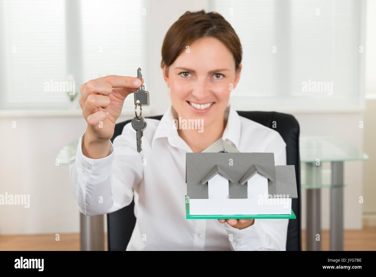 Felice imprenditrice in possesso della chiave e il modello della casa in ufficio Foto Stock