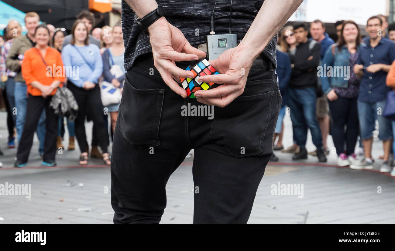 Una strada mago comico intrattiene i turisti nel cuore di Leicester Square completando un cubo di Rubik puzzle dietro il suo dorso entro pochi secondi. Foto Stock