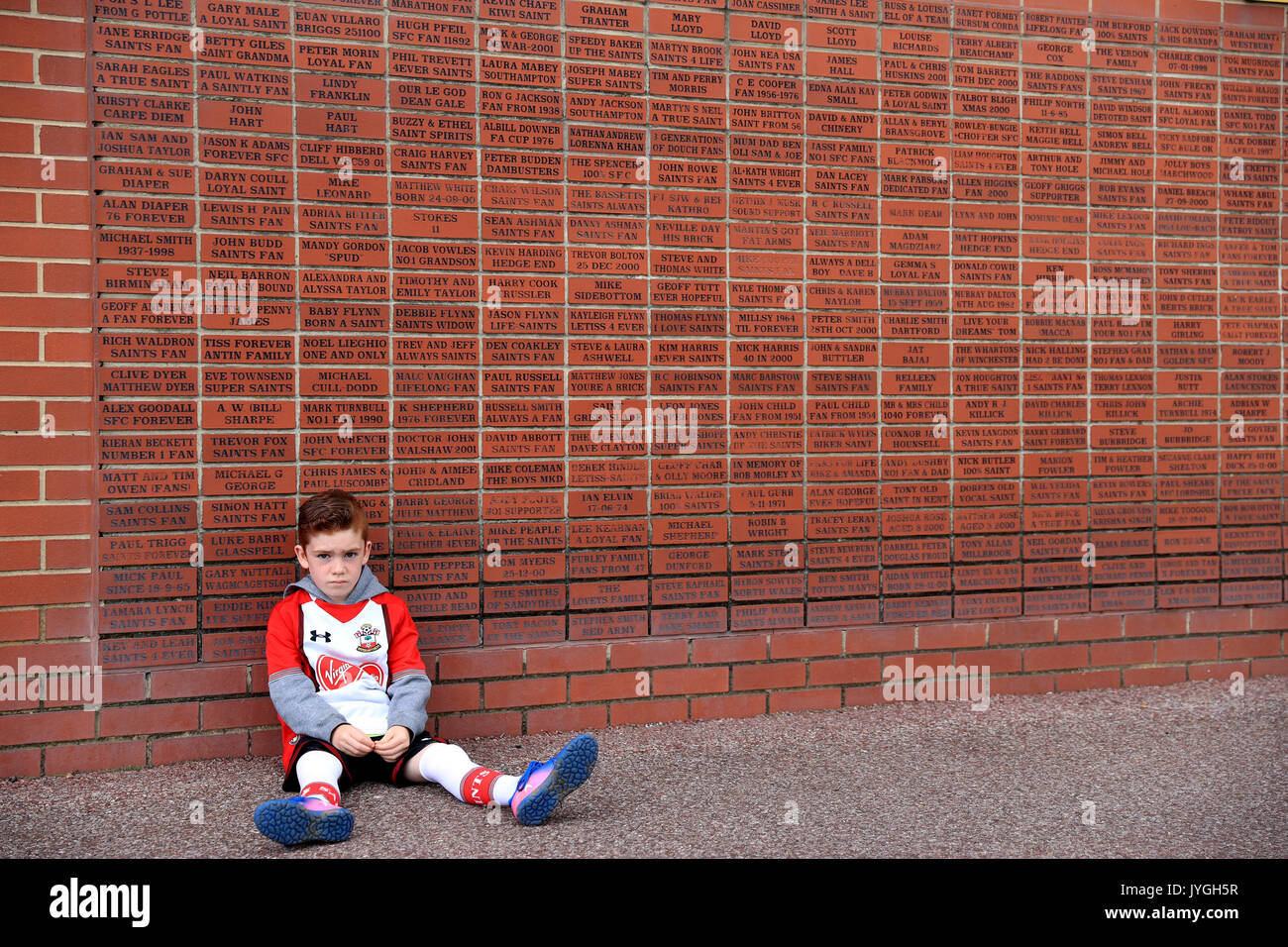 Un giovane Southampton ventola accanto a un mattone memorial wall prima della Premier League a St Mary's, Southampton. Foto Stock