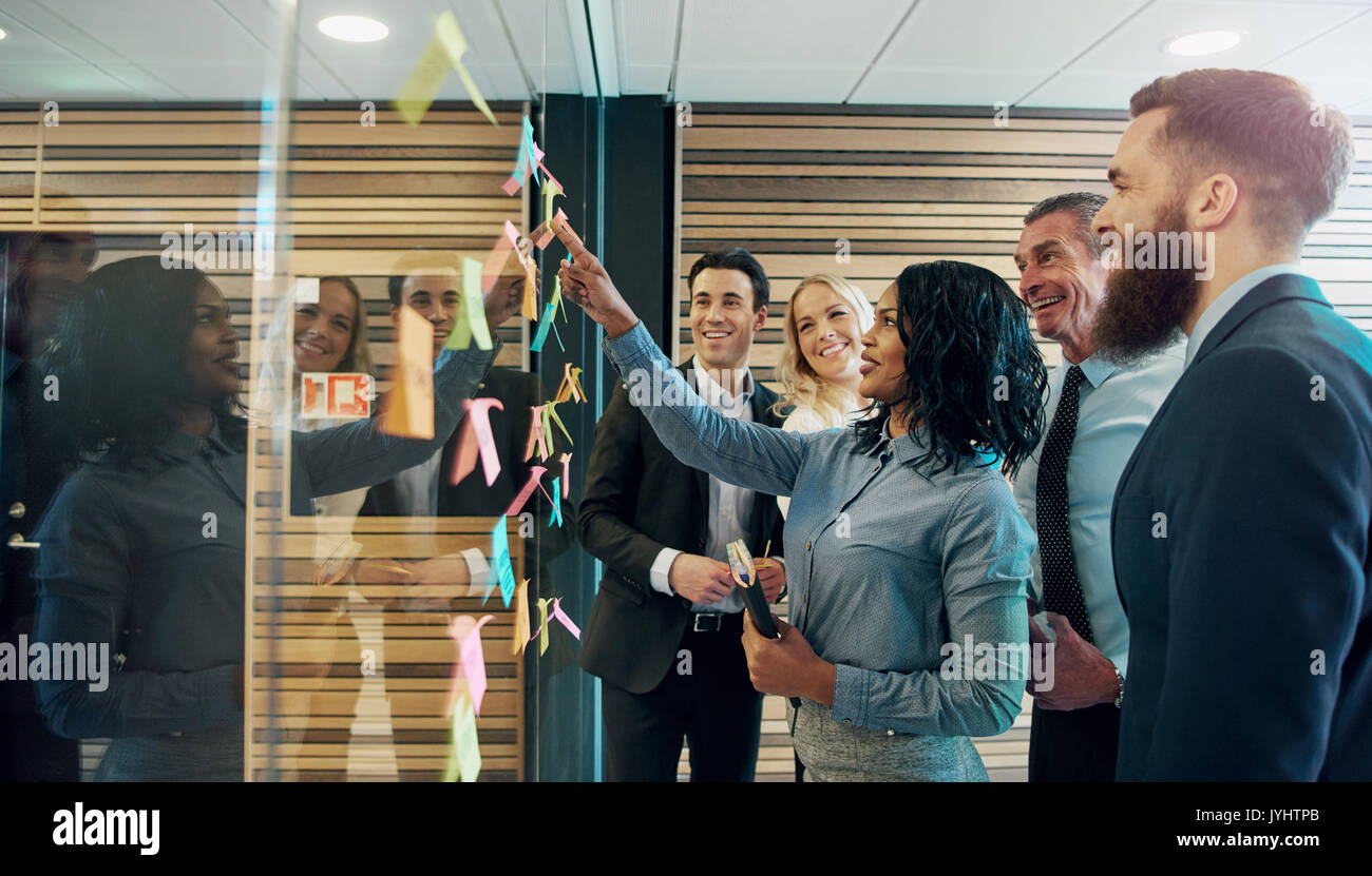 Felice imprenditori creativi di brainstorming in office, mettendo sticky notes con idee su vetro Foto Stock
