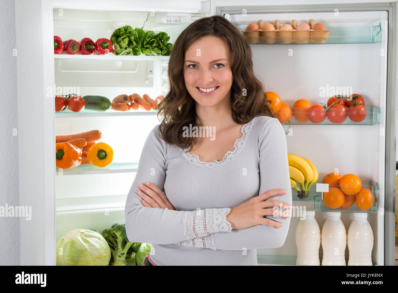 Giovane donna felice con Armcrossed davanti di aprire il frigo con cibo sano Foto Stock