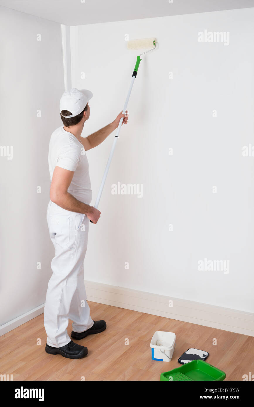 Giovane pittore in bianco uniforme pittura con rullo di vernice sulla parete Foto Stock