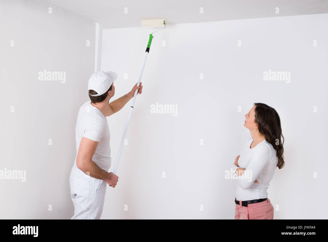 Giovane donna guardando il pittore pittura bianca sulla parete in casa Foto Stock