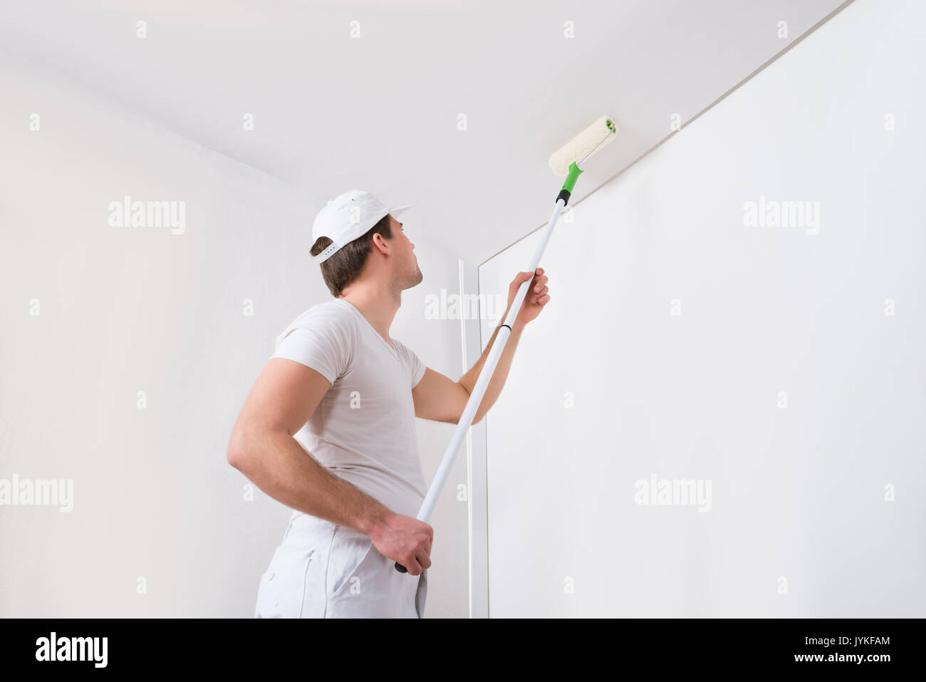 Giovane pittore in bianco uniforme pittura con rullo di vernice sulla parete Foto Stock