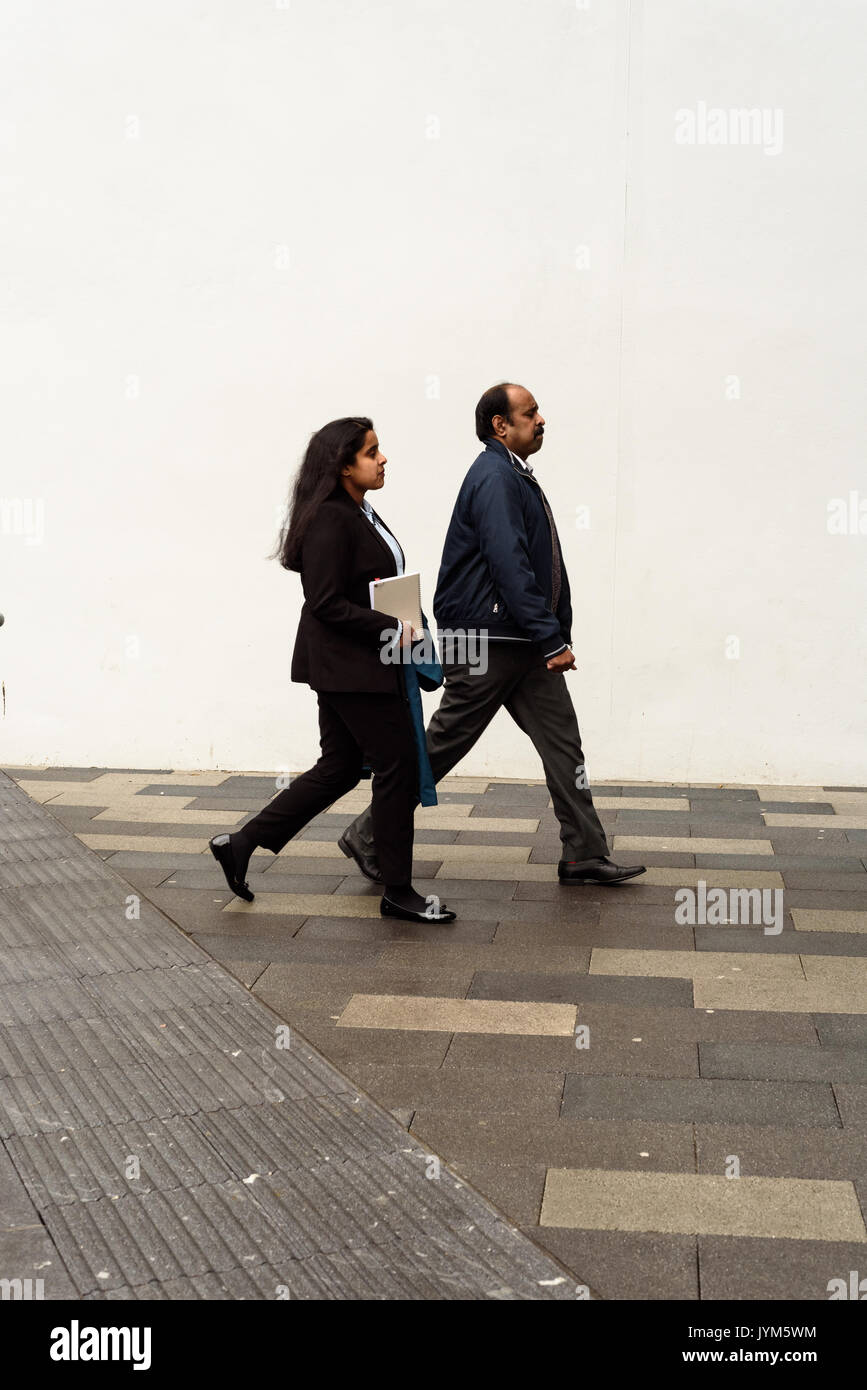 Giovane ragazza asiatica e il vecchio uomo che cammina lungo un umido pavimento piastrellato con un muro bianco sfondo in Inghilterra Foto Stock