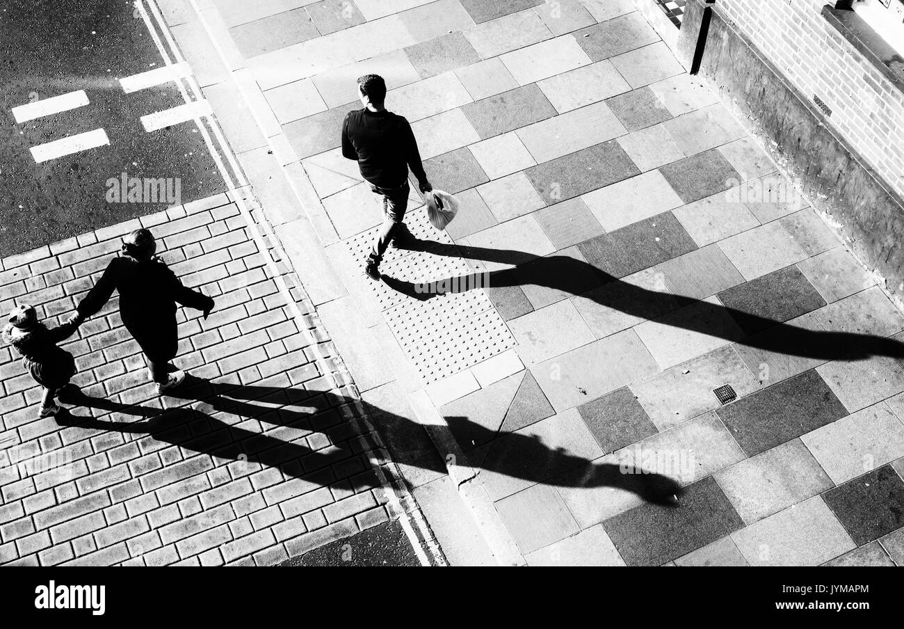 Uomo Donna e bambino attraversare la strada in direzione di un marciapiede con lunghe ombre forte ripresa dall'alto direttamente in testa Foto Stock