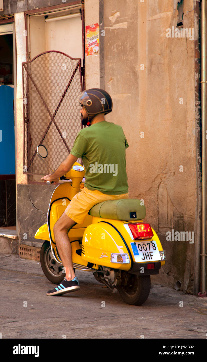 Uomo di salire sul giallo scooter indossare pantaloncini giallo e verde tee shirt a Toledo Spagna Foto Stock