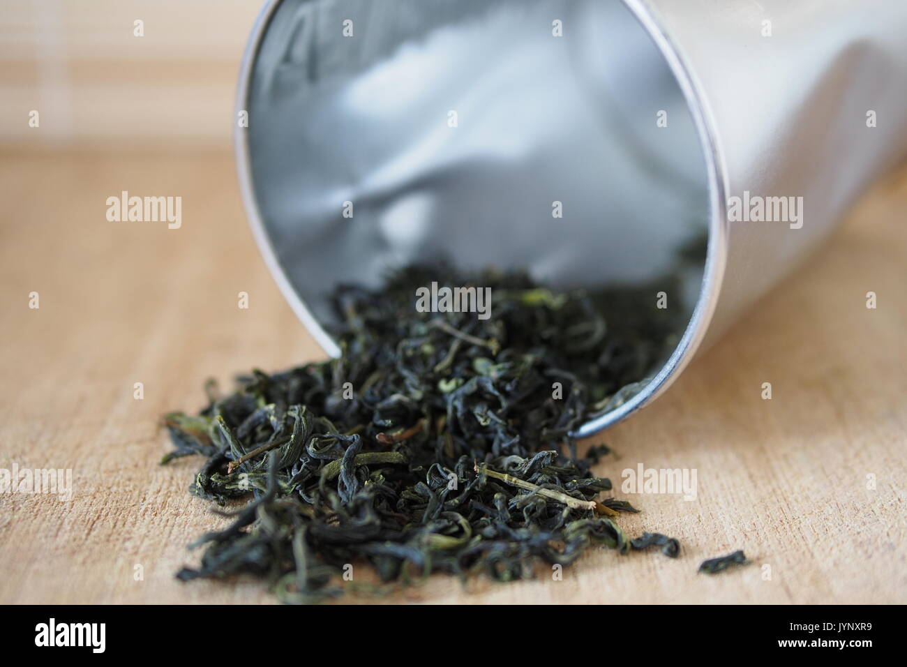 Essiccato il tè verde (Camellia sinensis) lascia la fuoriuscita da un argento stagno su un tagliere di legno. Foto Stock