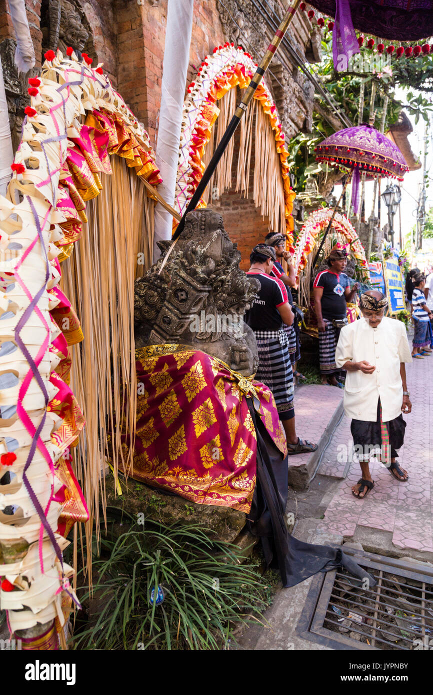 Uomo Balinese in abiti tradizionali, guardando un telefono cellulare durante un Royal cremazione in Ubud, Bali. Decorazioni colorate sulla sinistra. Formato verticale. Foto Stock
