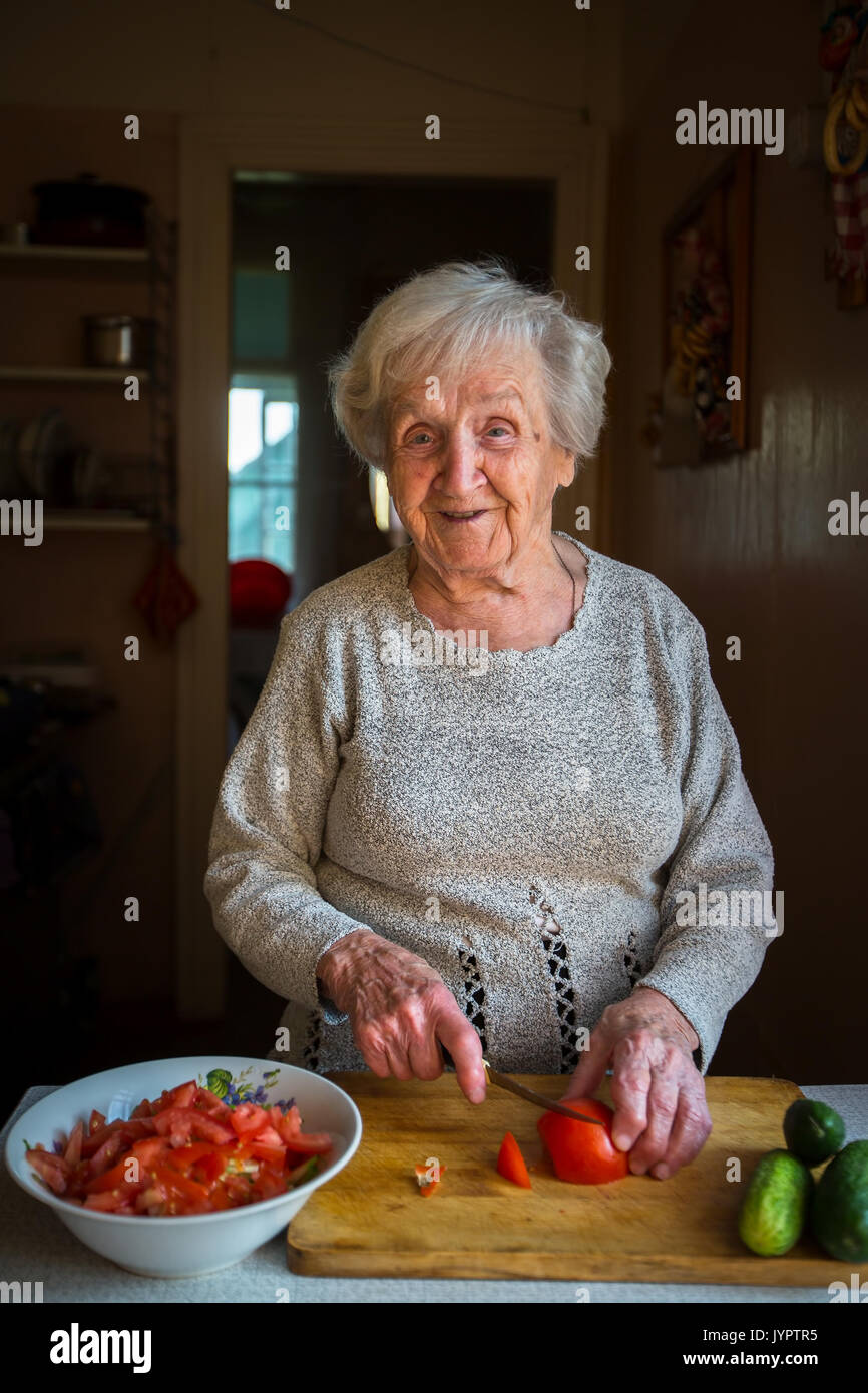 Una donna anziana trita verdure per insalata in cucina. Foto Stock