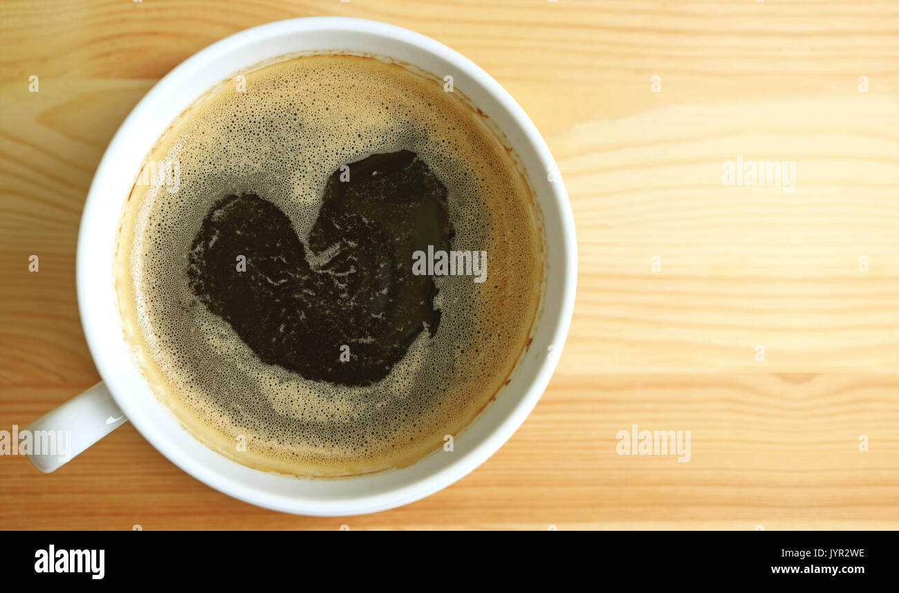 Forma di cuore caldo caffè nero schiuma, vista dall'alto con spazio libero sul tavolo di legno per testo e design Foto Stock