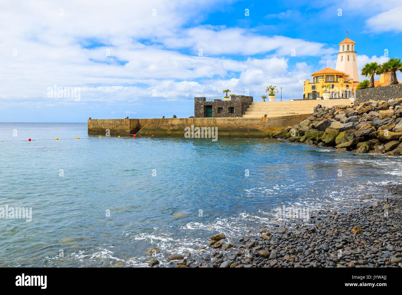 Ghiaiosa spiaggia di pietra e edificio del faro sulla costa dell'isola di Madeira, Portogallo Foto Stock