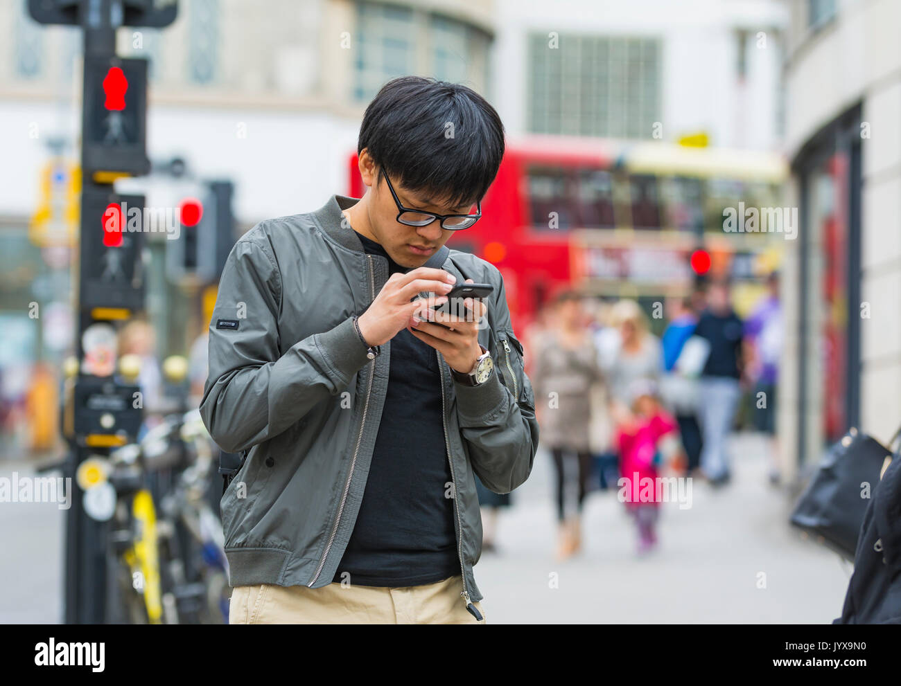 Giovane uomo giapponese in una città del Regno Unito verifica il suo smartphone mentre fuori. Foto Stock