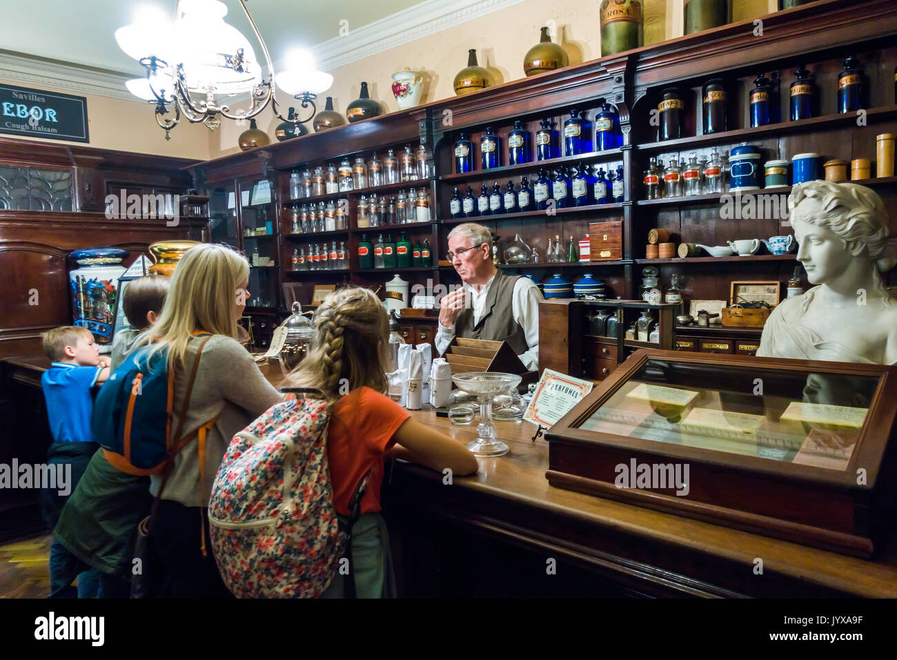 Interno di un inizio del XIX secolo Pharmacy store nella città di Kirkgate nel Museo del Castello di York con un assistente maschio e quattro bambini in visita Foto Stock