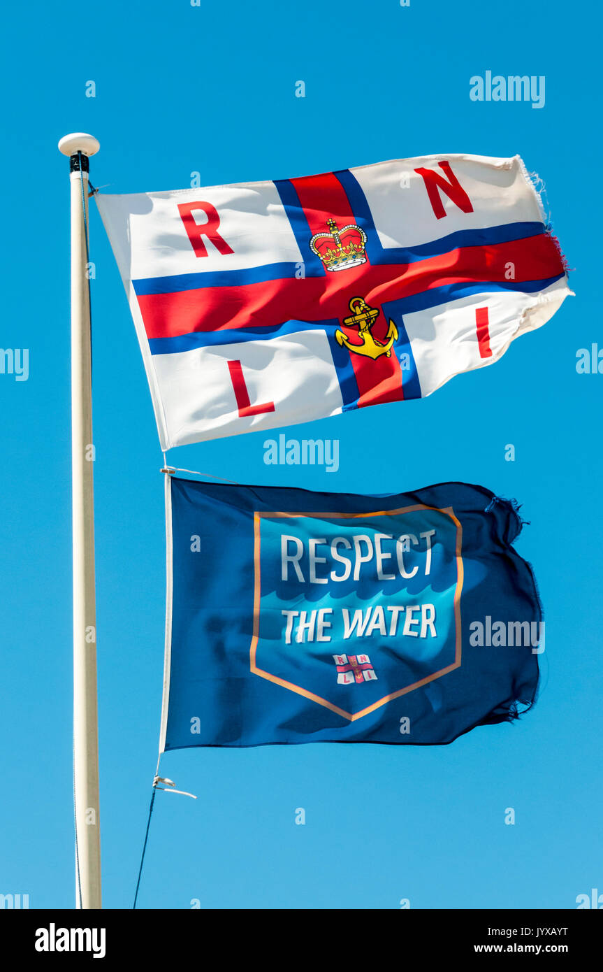 RNLI & rispetto l'acqua bandiere che sventolano fuori la Dungeness scialuppa di salvataggio stazione. Foto Stock