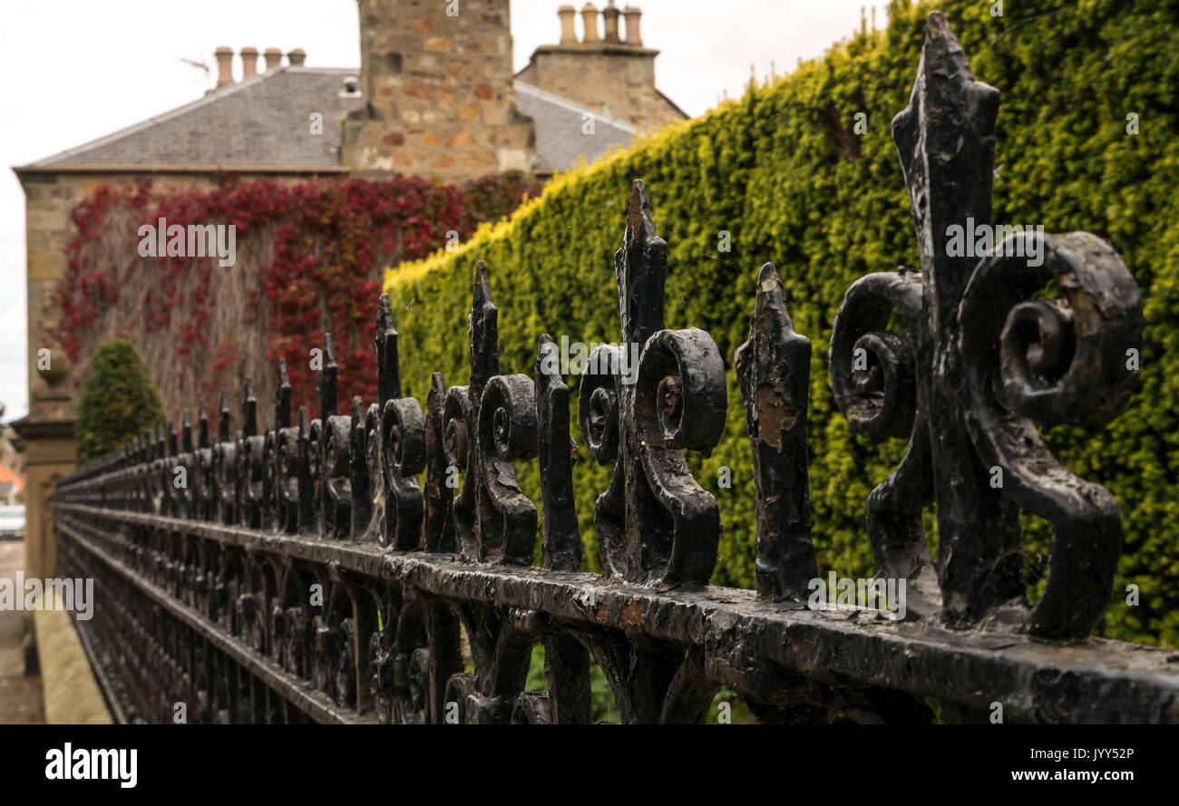 Vista obliqua lungo ornati ringhiere Vittoriano, High Street, a Aberlady, East Lothian, Scozia, con muro di pietra coperto di edera rossa Foto Stock