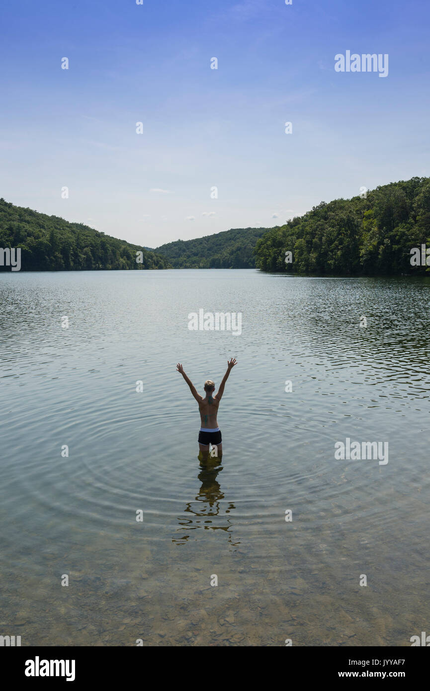 Donna con braccia alzate in piedi nel lago Foto Stock