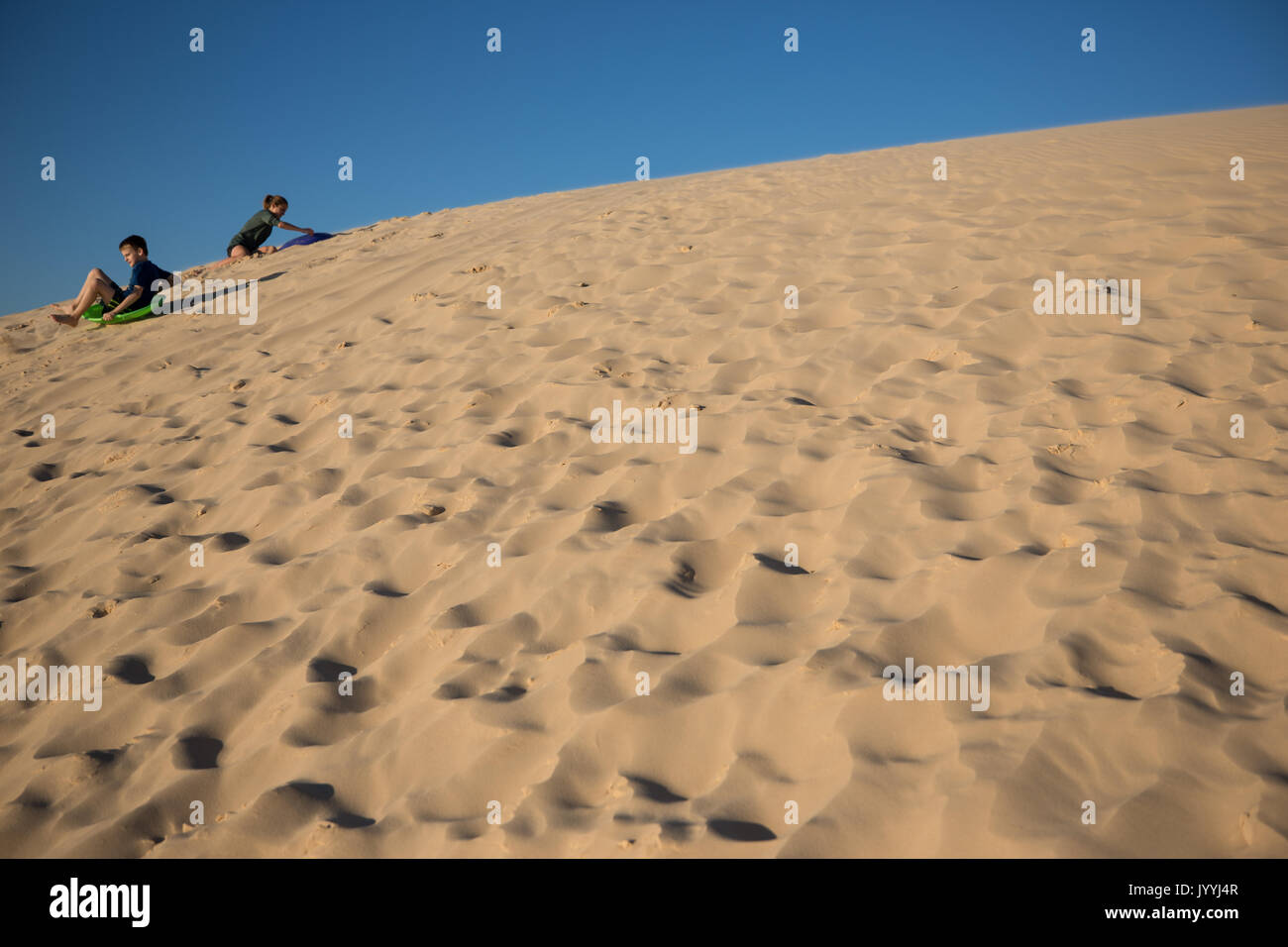 Teenage fratello e sorella di scivolare verso il basso le dune di sabbia Foto Stock