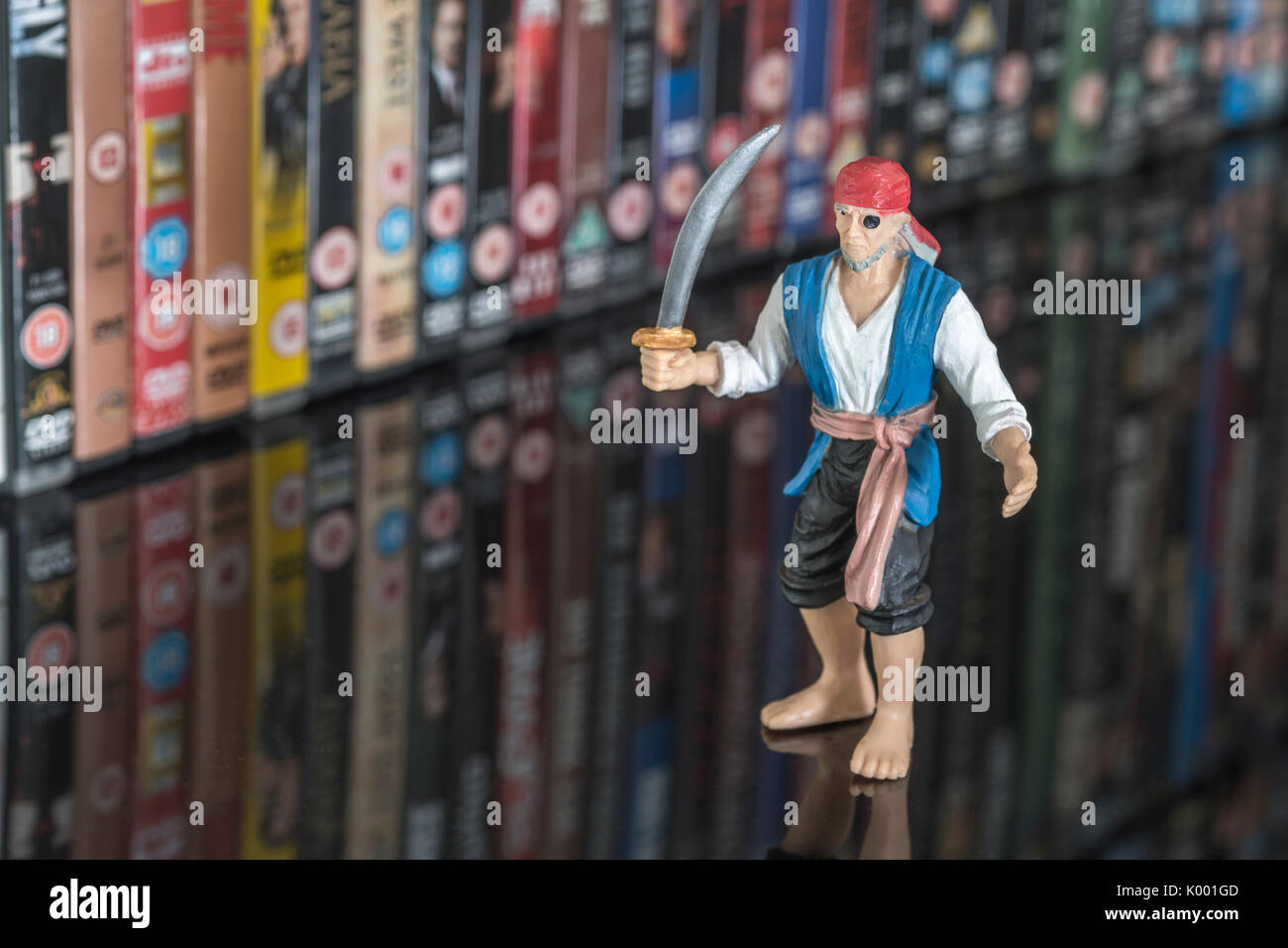 La spada wielding pirata giocattolo in piedi di fronte a pile di DVD (Disco versatile digitale) - metafora della pirateria del software, Cinese merci contraffatte, furto di IP Foto Stock