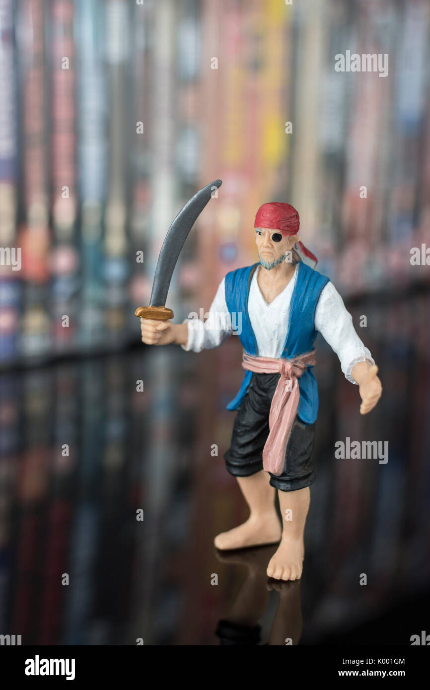 La spada wielding pirata giocattolo in piedi di fronte a pile di DVD (Disco versatile digitale) - metafora della pirateria del software, Cinese merci contraffatte, furto di IP Foto Stock