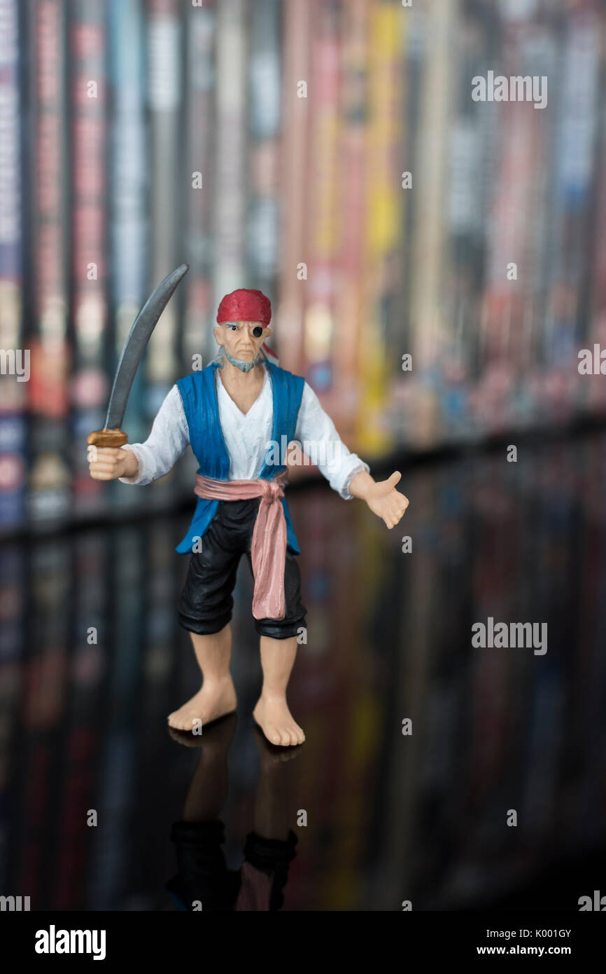 La spada wielding pirata giocattolo in piedi di fronte a pile di DVD (Disco versatile digitale) - metafora della pirateria del software, Cinese merci contraffatte, furto di IP Foto Stock