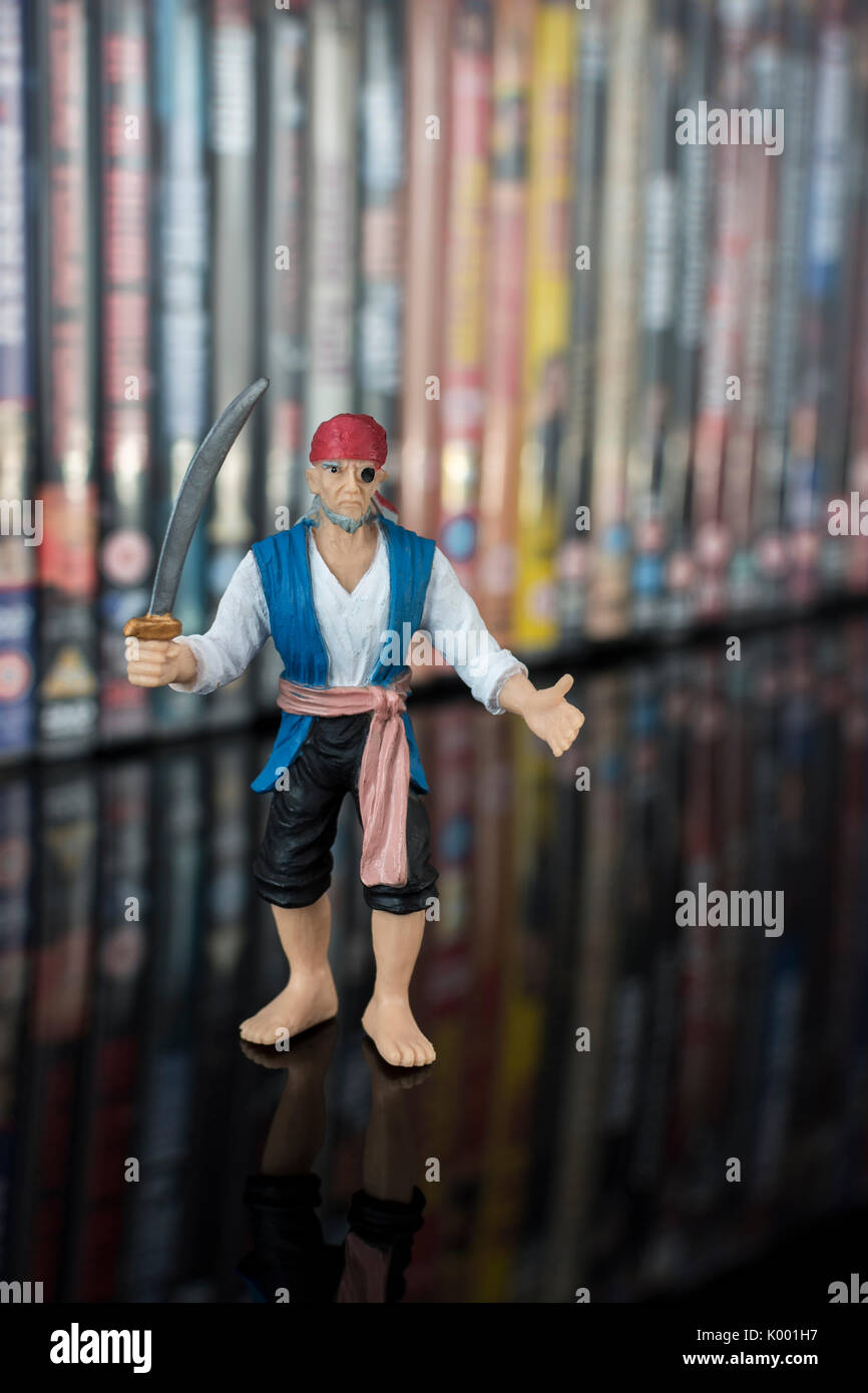 La spada wielding pirata giocattolo in piedi di fronte a pile di DVD (Disco versatile digitale) - metafora della pirateria del software, Cinese merci contraffatte, furto di IP Foto Stock