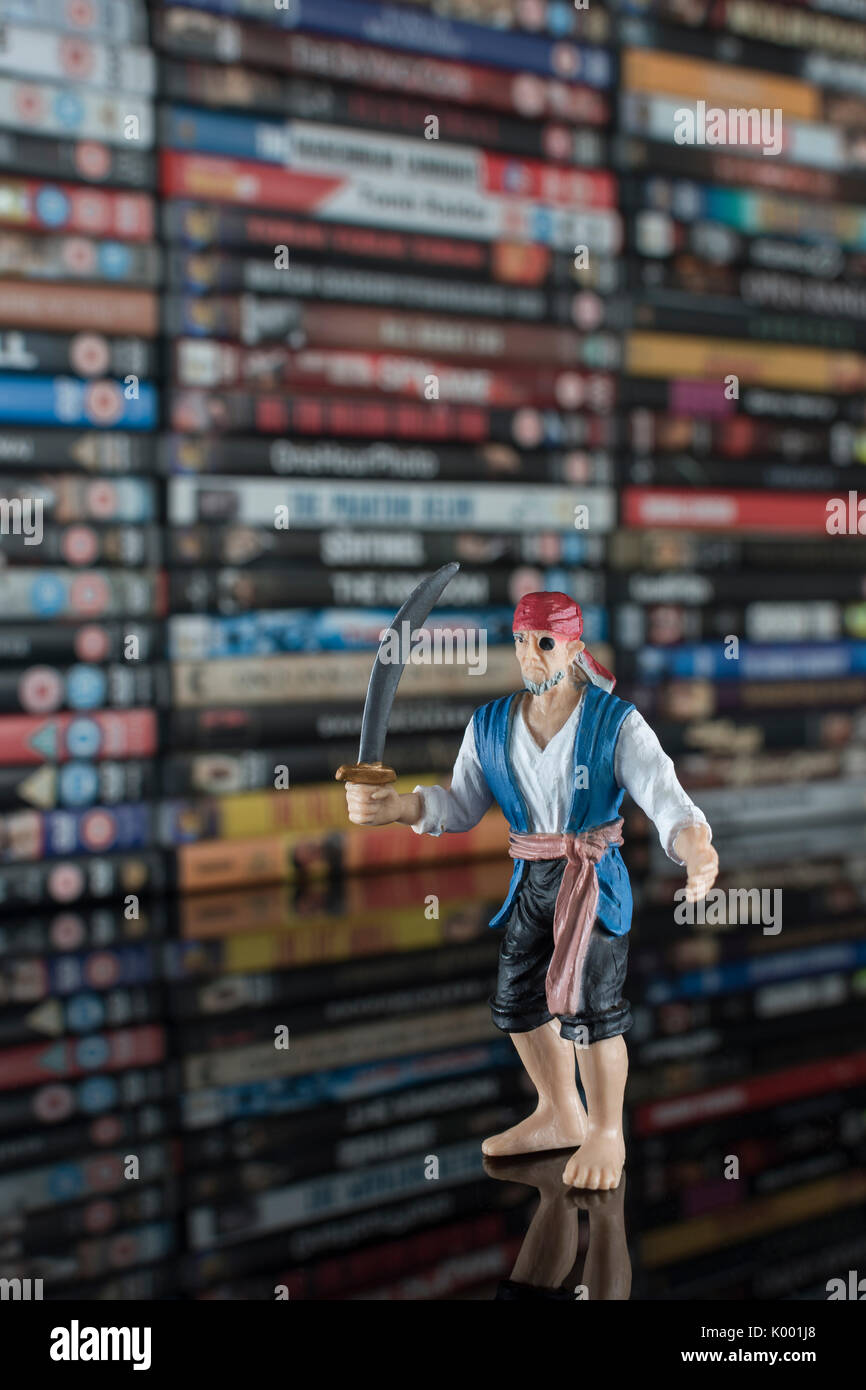 La spada wielding pirata giocattolo in piedi di fronte a pile di DVD (Disco versatile digitale) - metafora della pirateria del software, Cinese merci contraffatte, furto di IP Foto Stock