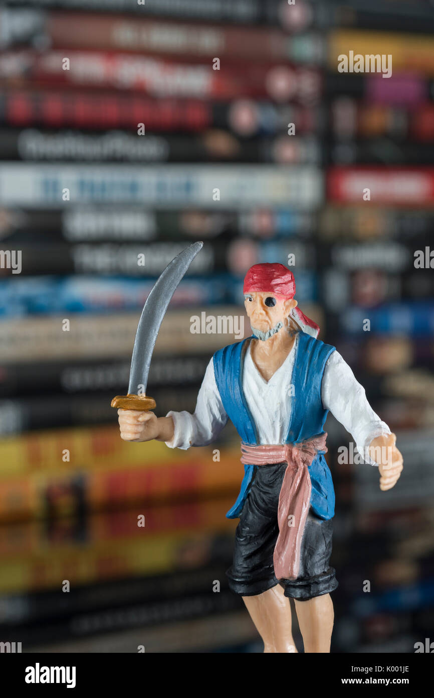 La spada wielding pirata giocattolo in piedi di fronte a pile di DVD (Disco versatile digitale) - metafora della pirateria del software, Cinese merci contraffatte, furto di IP Foto Stock