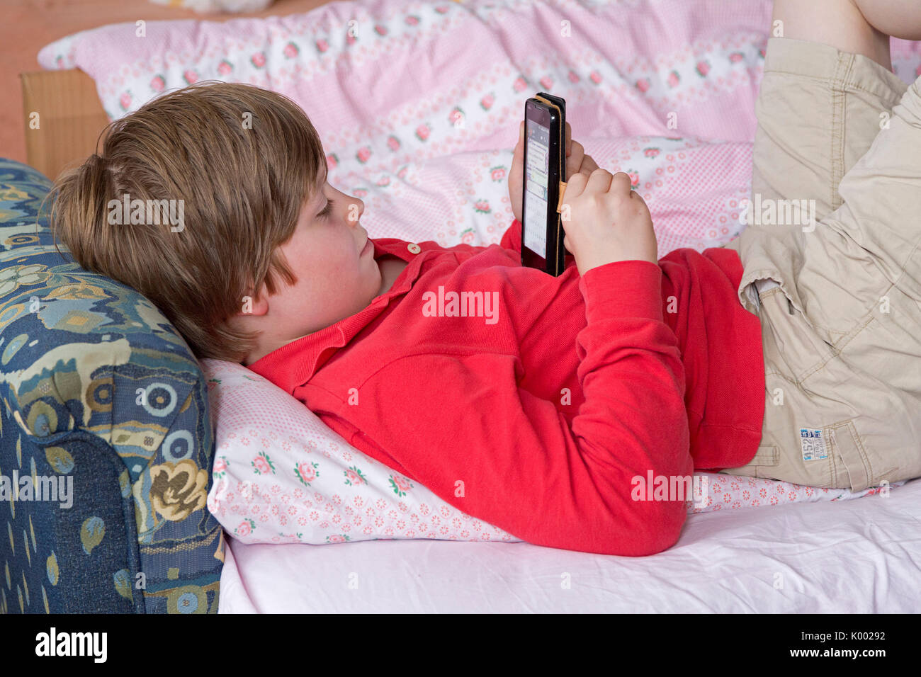 Giovane ragazzo disteso sul suo letto con il suo smartphone Foto Stock