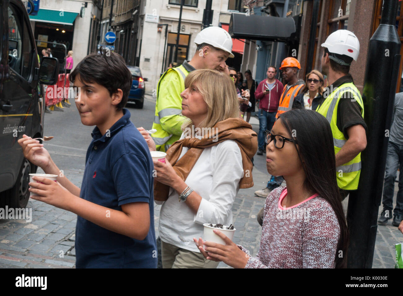 Persone che mangiano cibo di strada da vasche con operai sullo sfondo a Soho, Londra, Inghilterra, Regno Unito Foto Stock