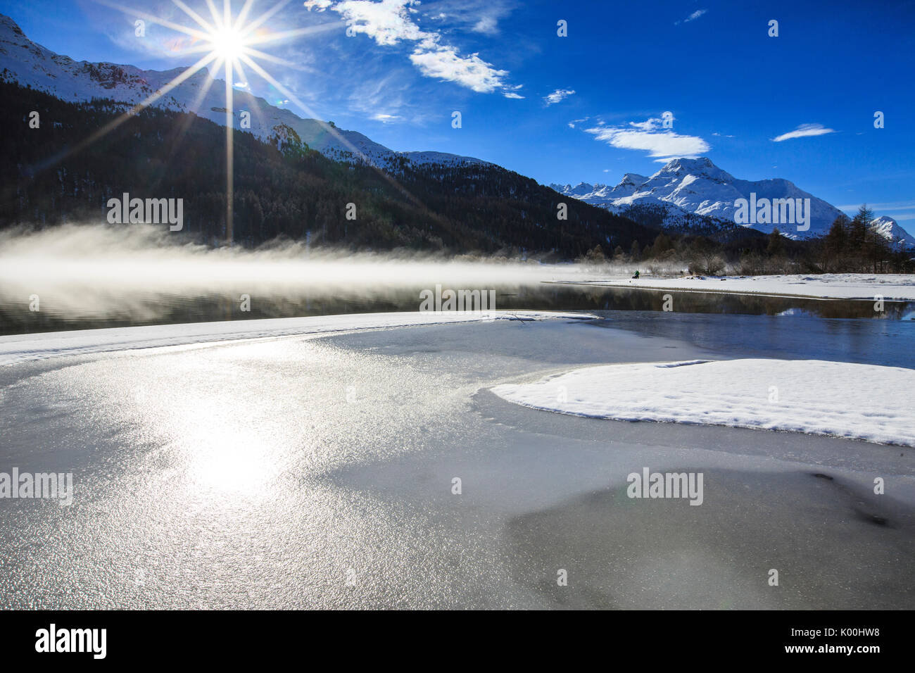 Inverno il sole illumina il lago ghiacciato di Silvaplana circondato da nebbia Maloja Cantone dei Grigioni Engadina Svizzera Europa Foto Stock