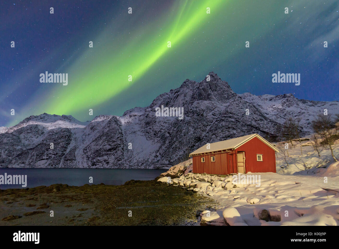 Northern Lights illuminare vette innevate e la cabina di legno su una notte stellata a Budalen Svolvaer Isole Lofoten in Norvegia Europa Foto Stock