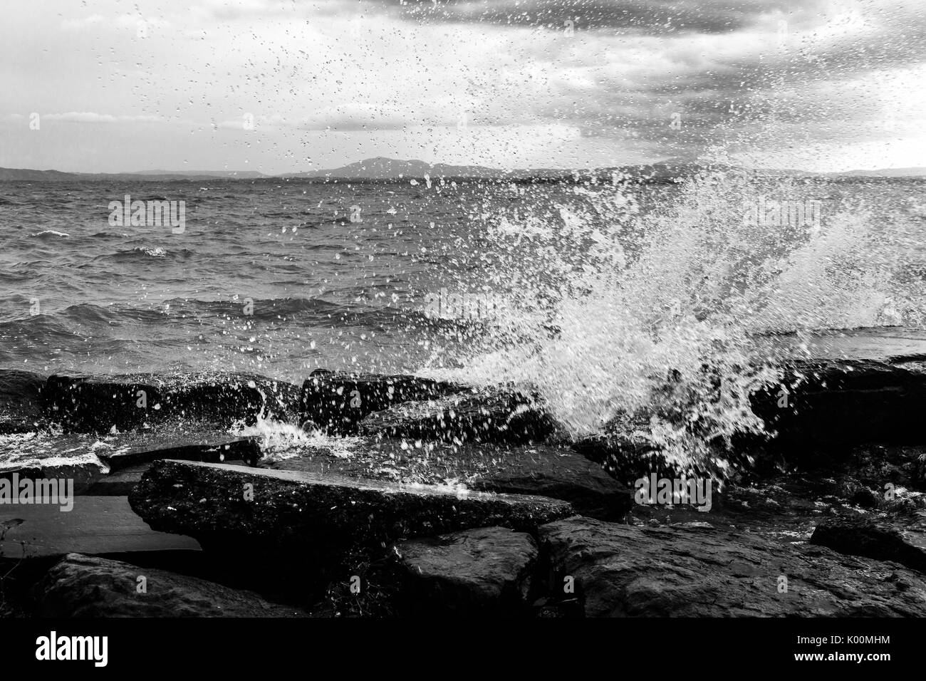 Vista ravvicinata di spruzzi d'acqua su rocce e sassi, sotto un cielo moody Foto Stock