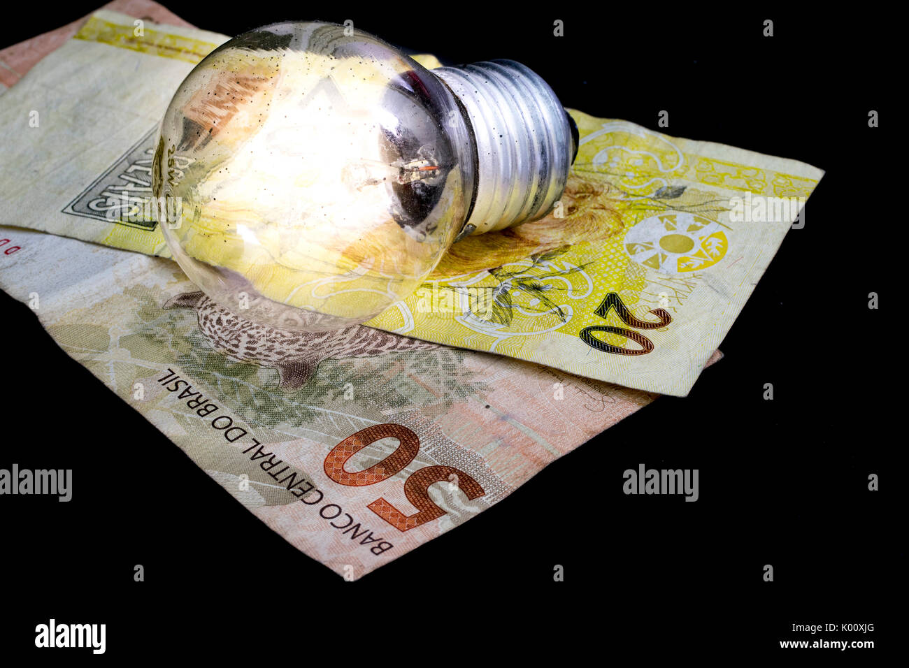 Due brasiliane denaro reale note, di 50 e 20 Valore, moneta del Brasile, su uno sfondo nero e una luce accesa la lampadina sulla parte superiore, come un idea di denaro e di concetto Foto Stock