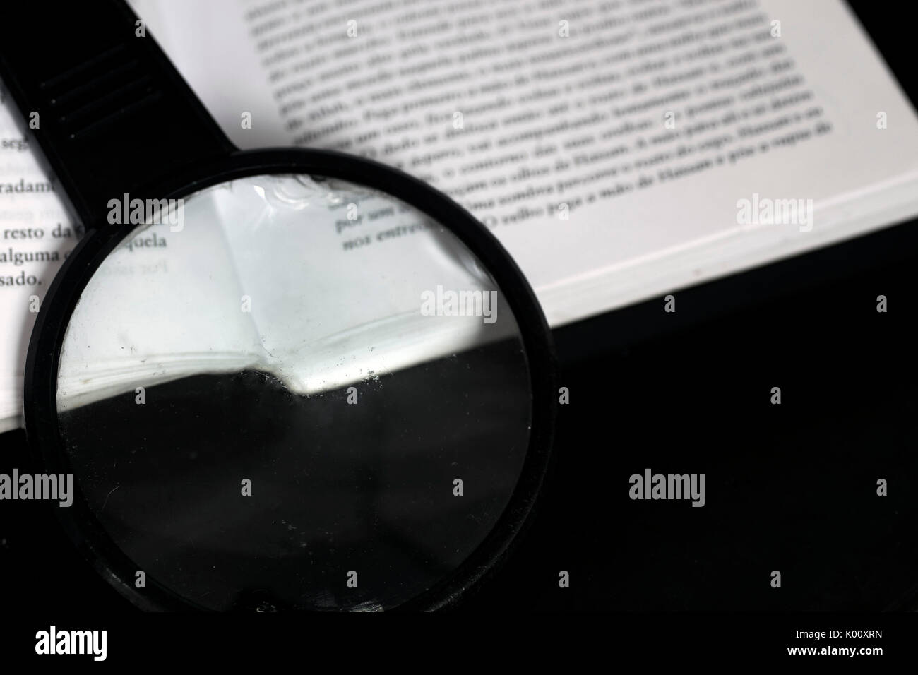 Lente di ingrandimento sulla parte superiore di un libro aperto sulla parte superiore di un nero riflettente la superficie di vetro Foto Stock