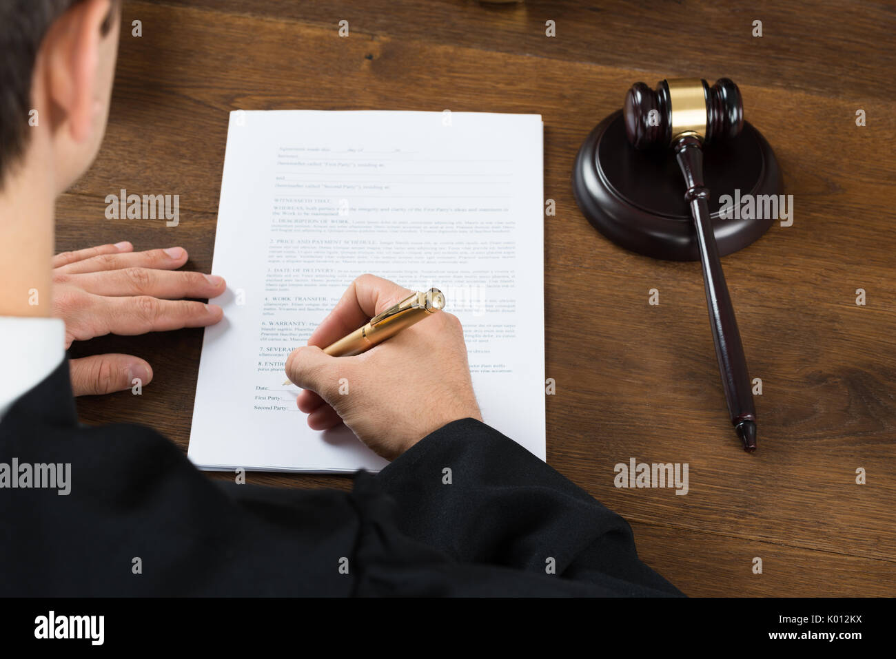 Angolo di alta vista del giudice maschio sulla scrittura di documenti legali al banco nelle aule di tribunale Foto Stock