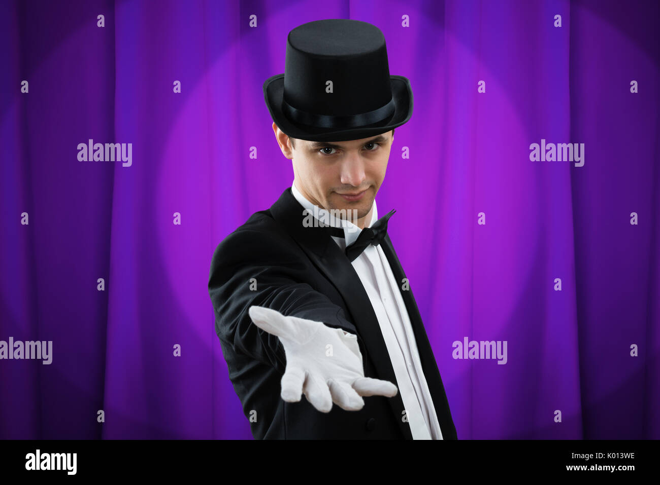 Ritratto di giovane mago maschio gesti contro la tenda viola Foto Stock
