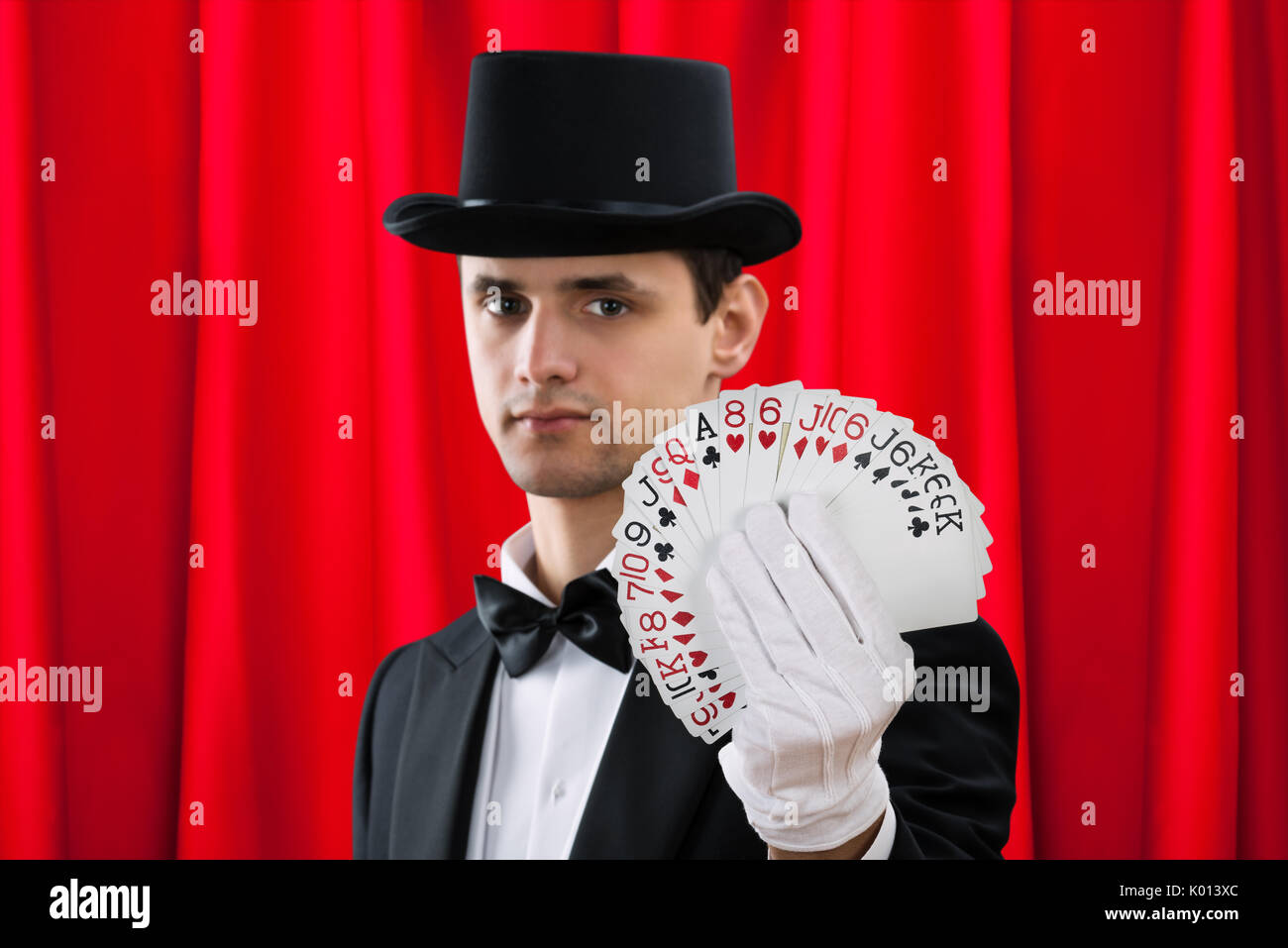 Ritratto di giovane mago maschio holding ventaglio carte contro il sipario rosso Foto Stock